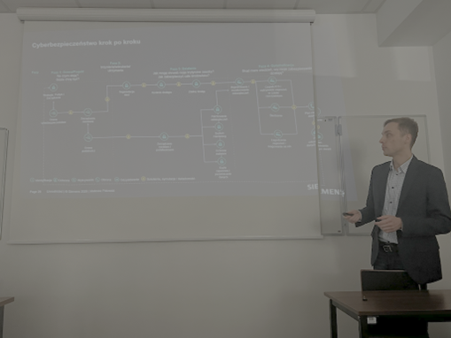 Mężczyzna stojący bokiem do ekranu i tłumaczący coś na podstawie obrazu z projektora