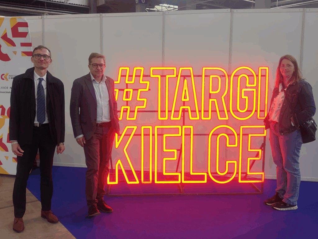 Dwcóch mężczyzn i kobieta stoją po obu stronach neonu Targi Kielce